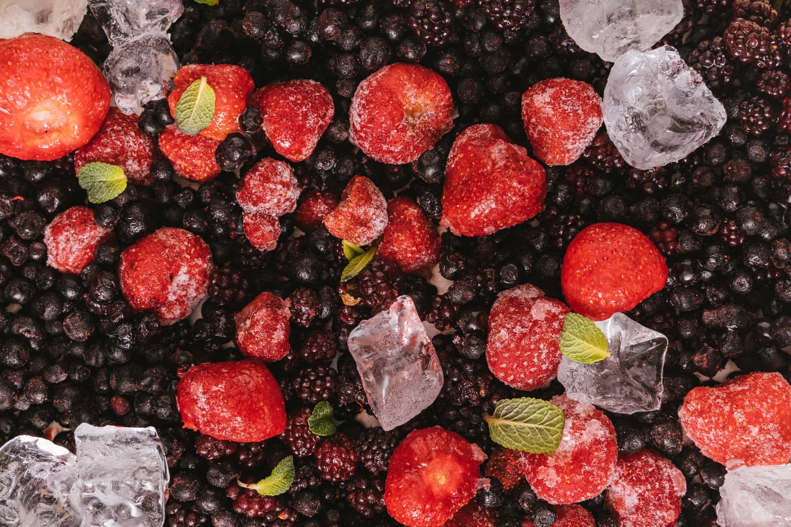 Frozen red berries and mint leaves photographed close up against a dark background
