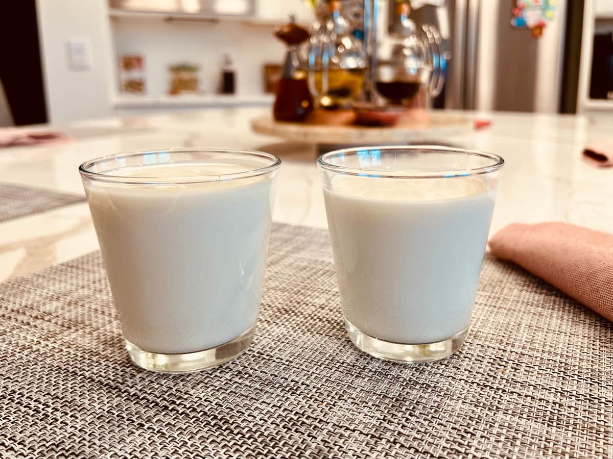 Two identical glasses of milk standing side by side on a kitchen table.