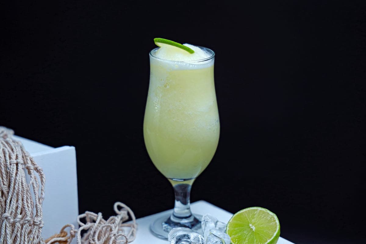 A tall glass of pale green citrus drink with lime slices and ice.